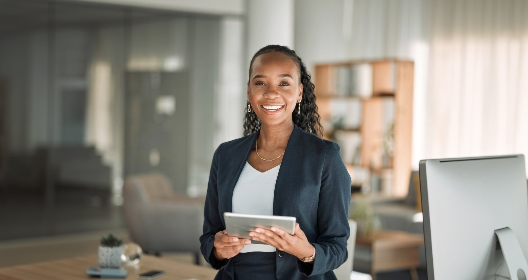 A professional standing at her desk with a tablet in a bright open-plan office